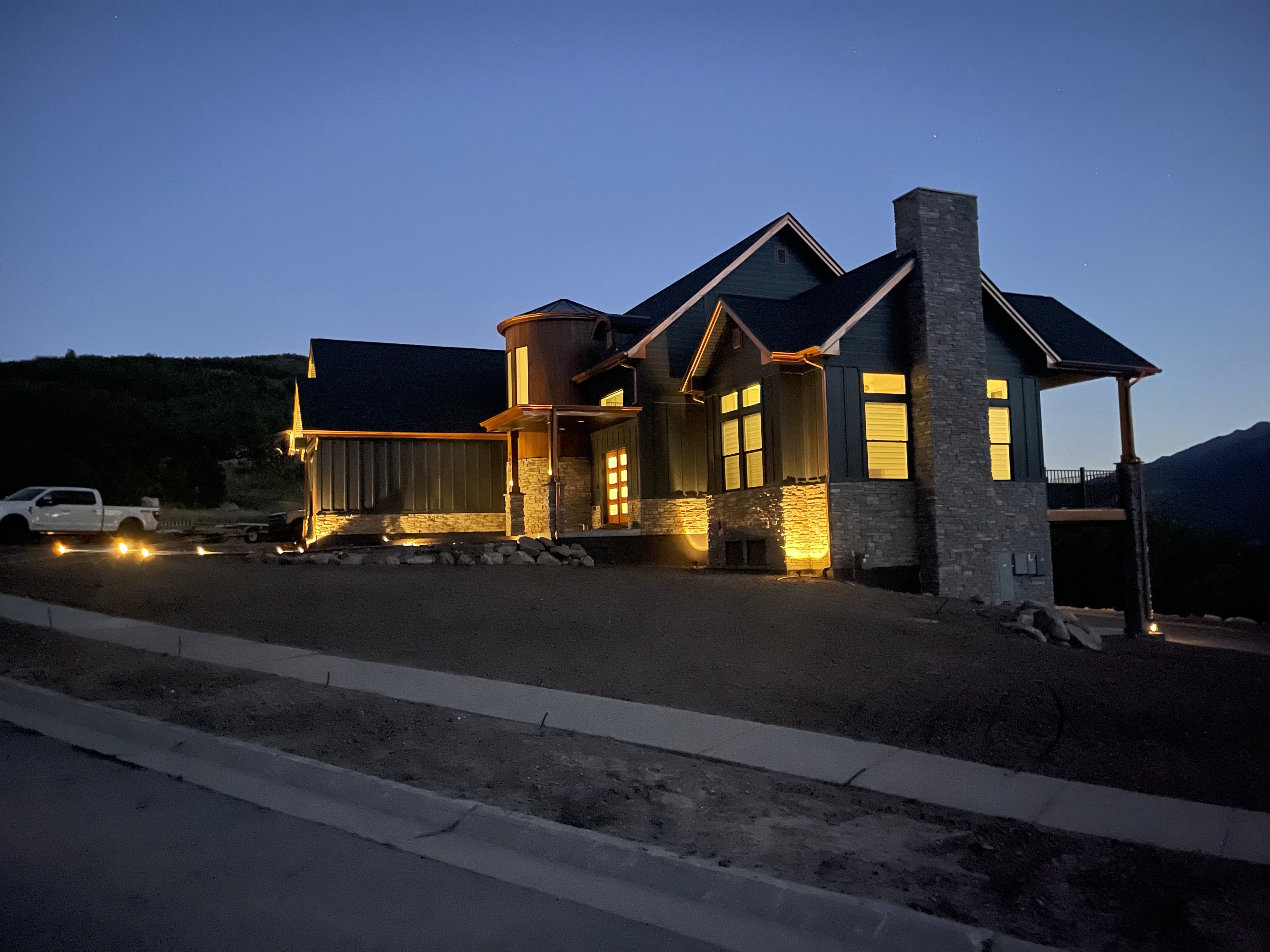 Custom home with stone chimney and landscape lighting at twilight